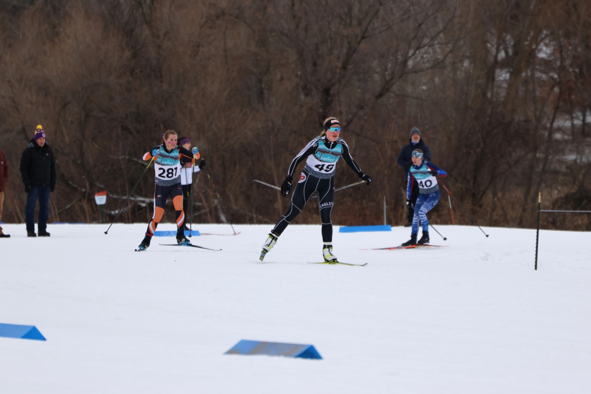 3 young women cross country skiers on snow-covered slope in front of tree line