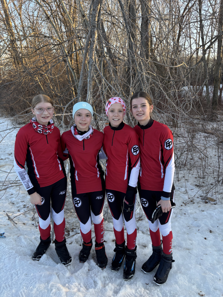 4 young teenage girls in red and black uniforms pose outdoors on snow in front of trees